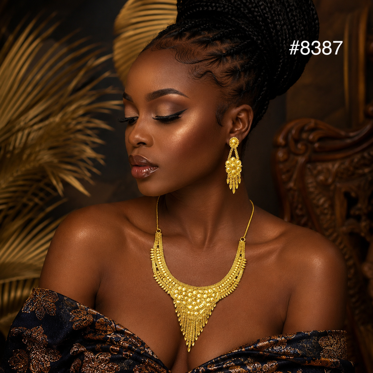 Elegant Black woman in profile wearing ornate gold jewelry and patterned dress, eyes lowered in a warm, regal portrait beside dried palm leaves.