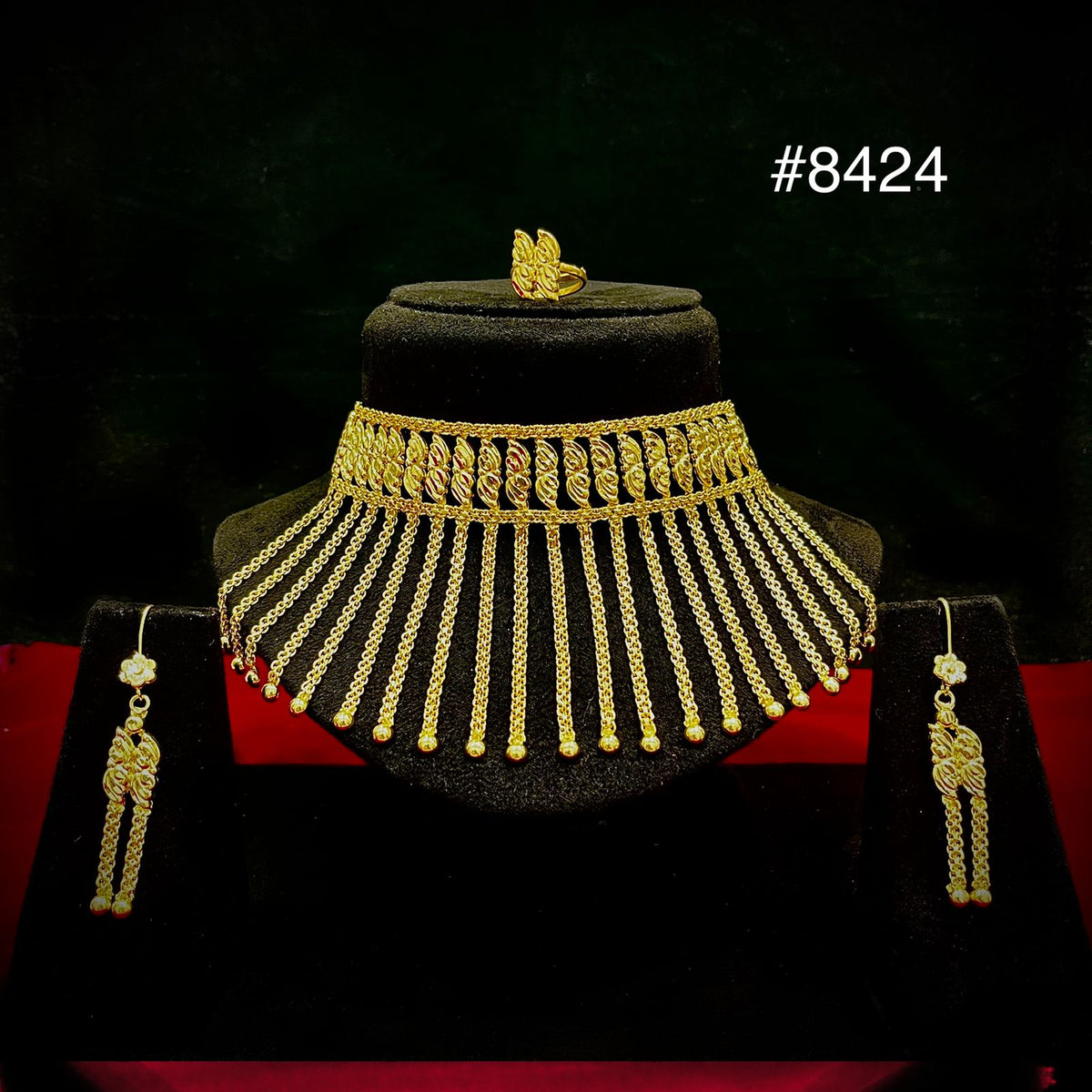Ornate gold necklace and matching earrings displayed on a black bust, with a butterfly ornament and dramatic red-and-black backdrop; #8424.