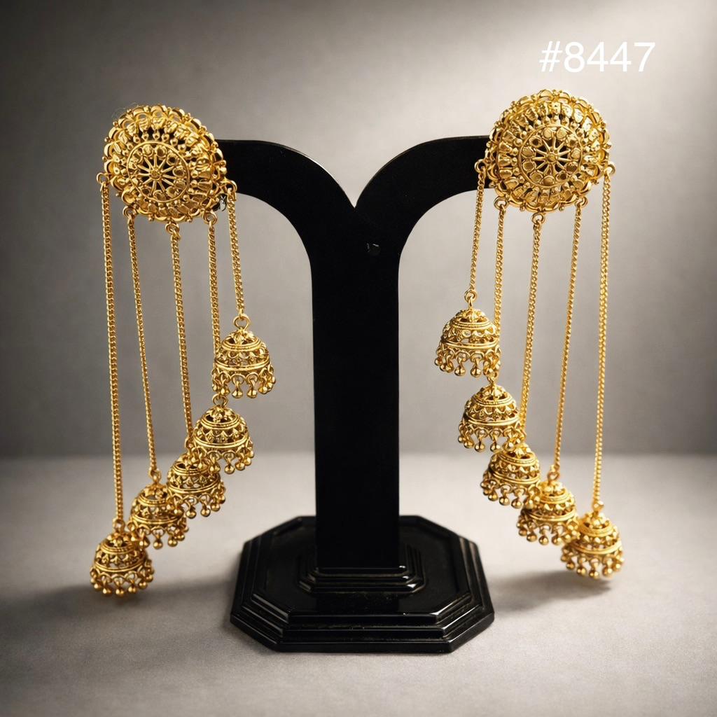 Ornate gold filigree chandelier earrings with long chains and dangling jhumka bells displayed symmetrically on a black stand, elegant and luxurious.