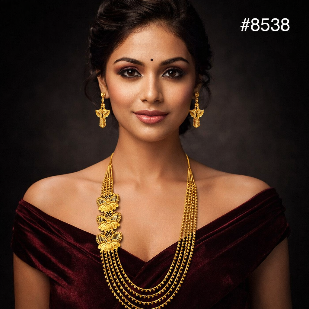 Portrait of a poised South Asian woman in a burgundy velvet sari, wearing ornate gold jewelry and a bindi against a dark backdrop.