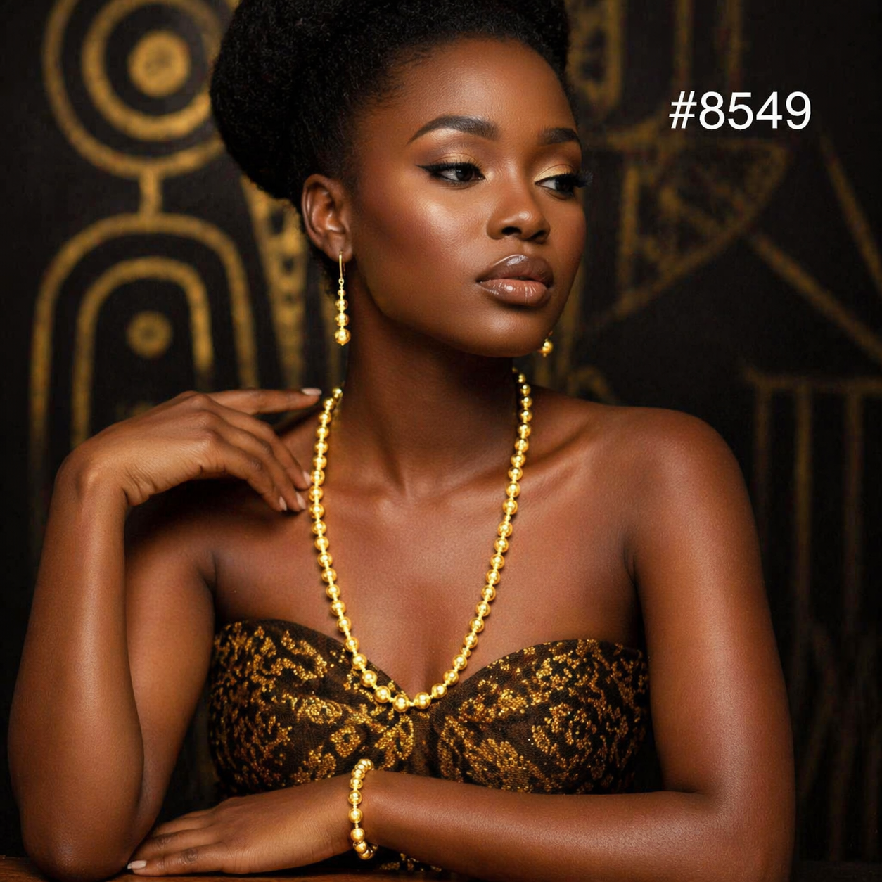 A woman with dark skin wears a gold bead necklace, matching earrings, and a bracelet, posing against a dark background with gold patterns and #8549.