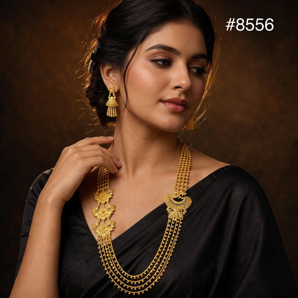Portrait of a poised woman in a black sari wearing ornate gold jewelry, looking aside against a warm brown backdrop with a graceful, elegant mood.