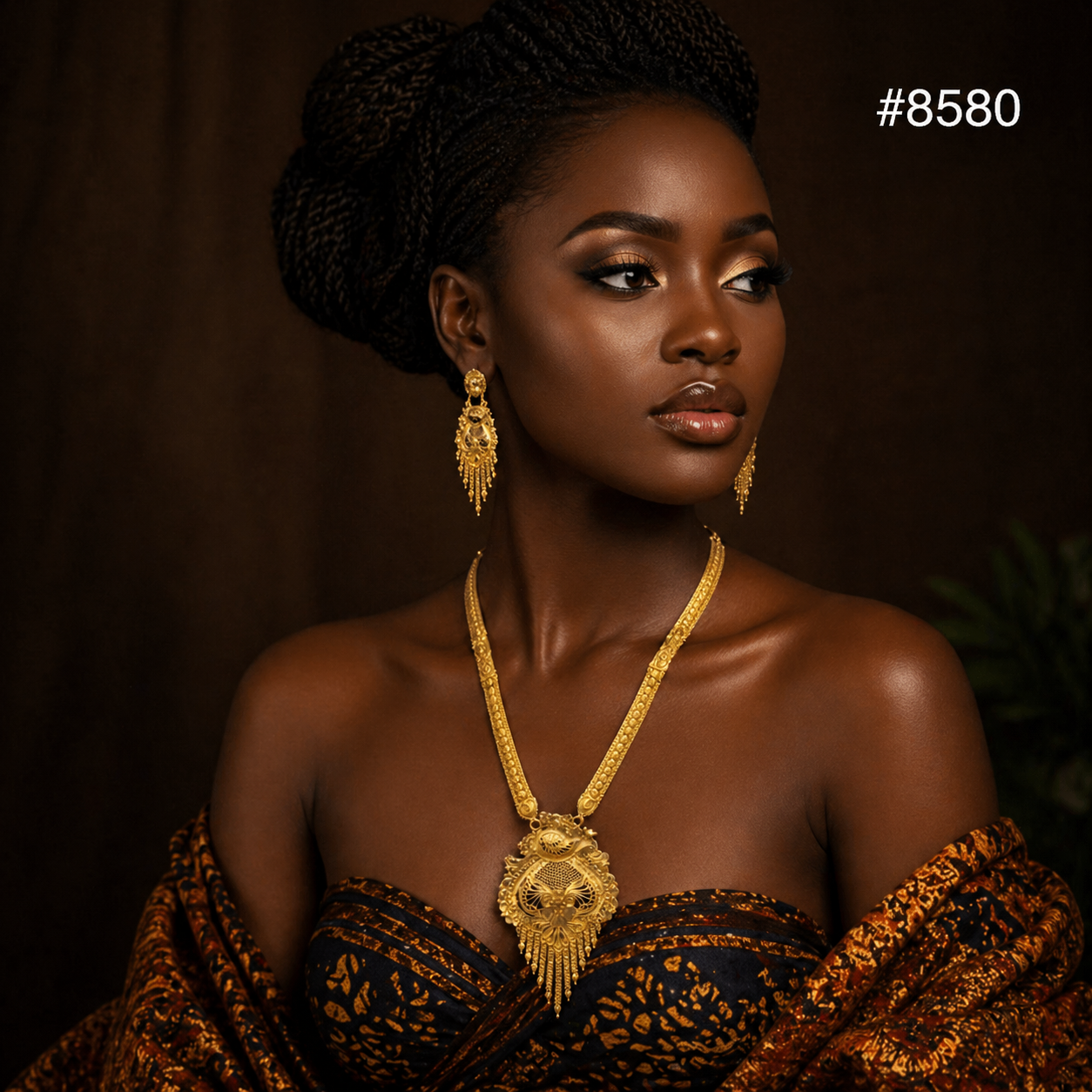A woman with dark skin and braided hair wears a gold filigree necklace and matching drop earrings, draped in a patterned brown and black fabric.