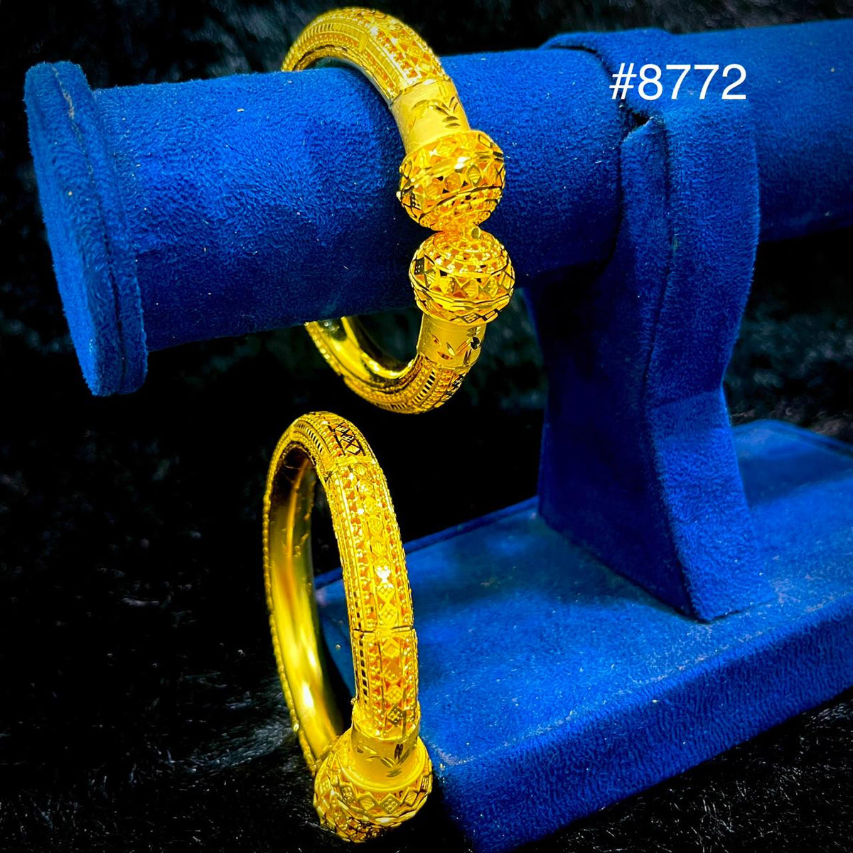 Two intricately designed gold bangles displayed on a blue velvet stand, with the number #8772 in white text at the top right corner.