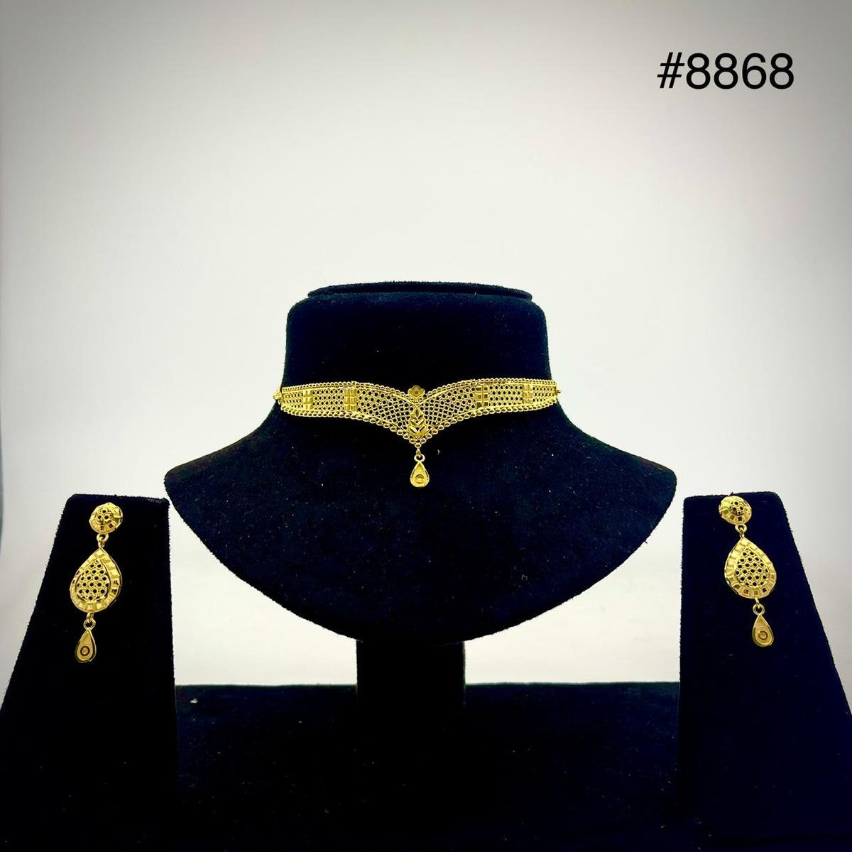 Gold filigree necklace with a teardrop pendant on a black velvet bust, flanked by matching dangling earrings; an elegant jewelry set.