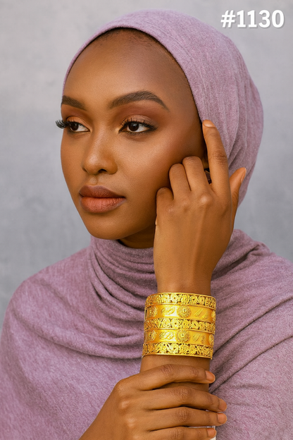 Portrait of a poised Black woman in a mauve hijab, wearing stacked gold bracelets and touching her headscarf against a gray backdrop.