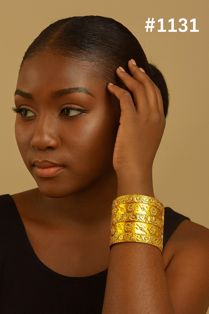Portrait of a Black woman with styled hair, wearing a black top and ornate gold cuff bracelet, touching her hair in a calm pose; #1131.