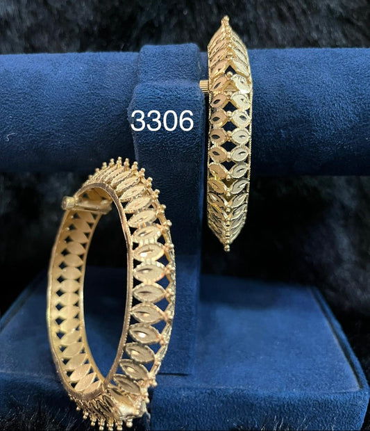 Two ornate gold hoop bangles with openwork diamond patterns and textured edges displayed on a blue velvet stand, marked “3306”; elegant jewelry presentation.