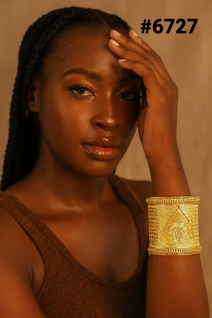 Portrait of a poised Black woman with braided hair, warm brown skin, and a gold cuff bracelet, touching her forehead in dramatic amber light.