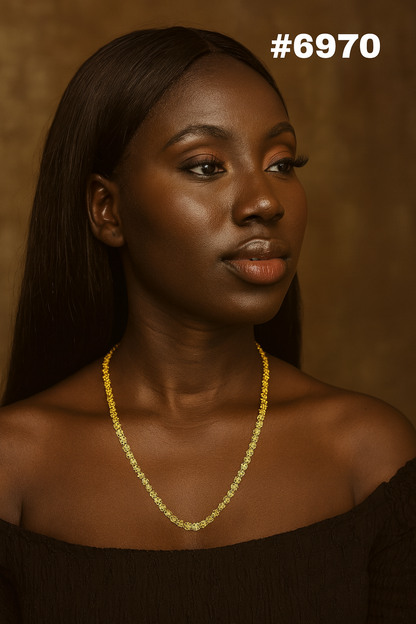 Portrait of a Black woman with long dark hair, wearing a delicate gold necklace and black off-shoulder top, gazing calmly right in warm light.
