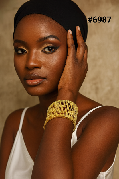 Portrait of a Black woman in a black headscarf and white camisole, touching her face; warm light highlights her makeup and gold cuff bracelet.