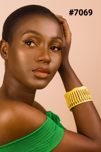 Portrait of a confident Black woman in a green off-shoulder top and ornate gold cuff, posing against a peach background; style label #7069.