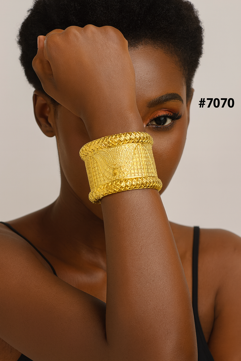 Close-up portrait of a confident Black woman covering one eye with her arm, showcasing an ornate wide gold cuff bracelet; label #7070.
