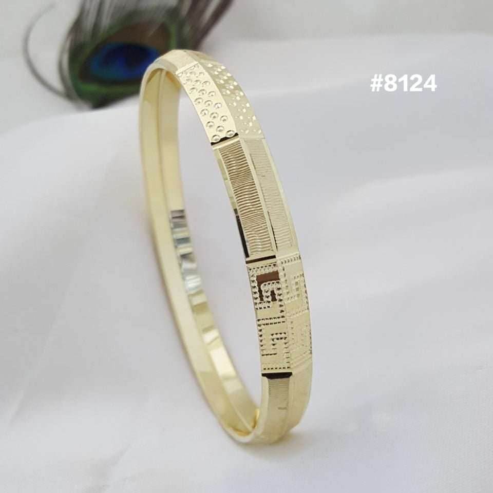 Gold bracelet on a white surface with a peacock feather in the background