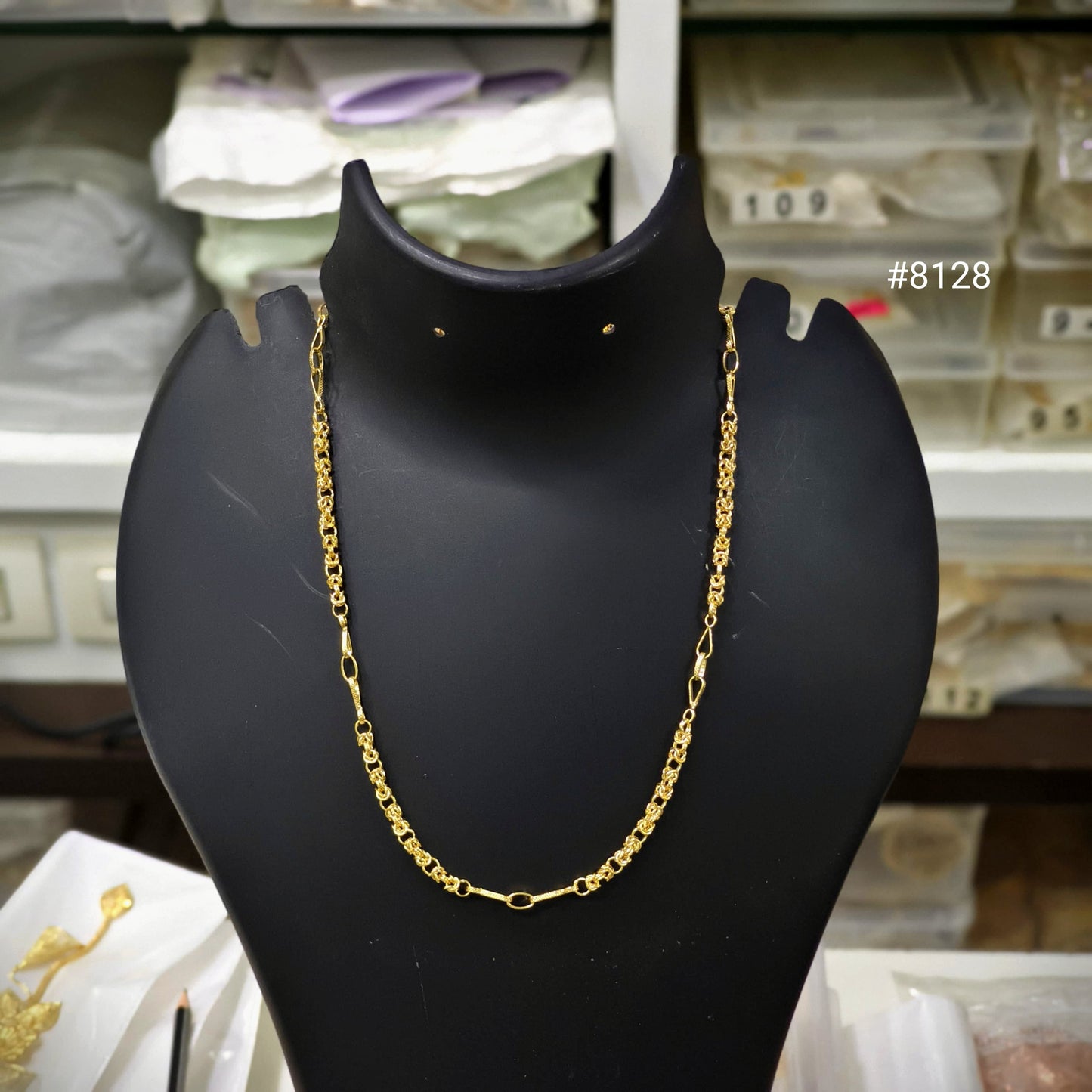 Gold chain necklace on a black mannequin bust with a blurred store background.
