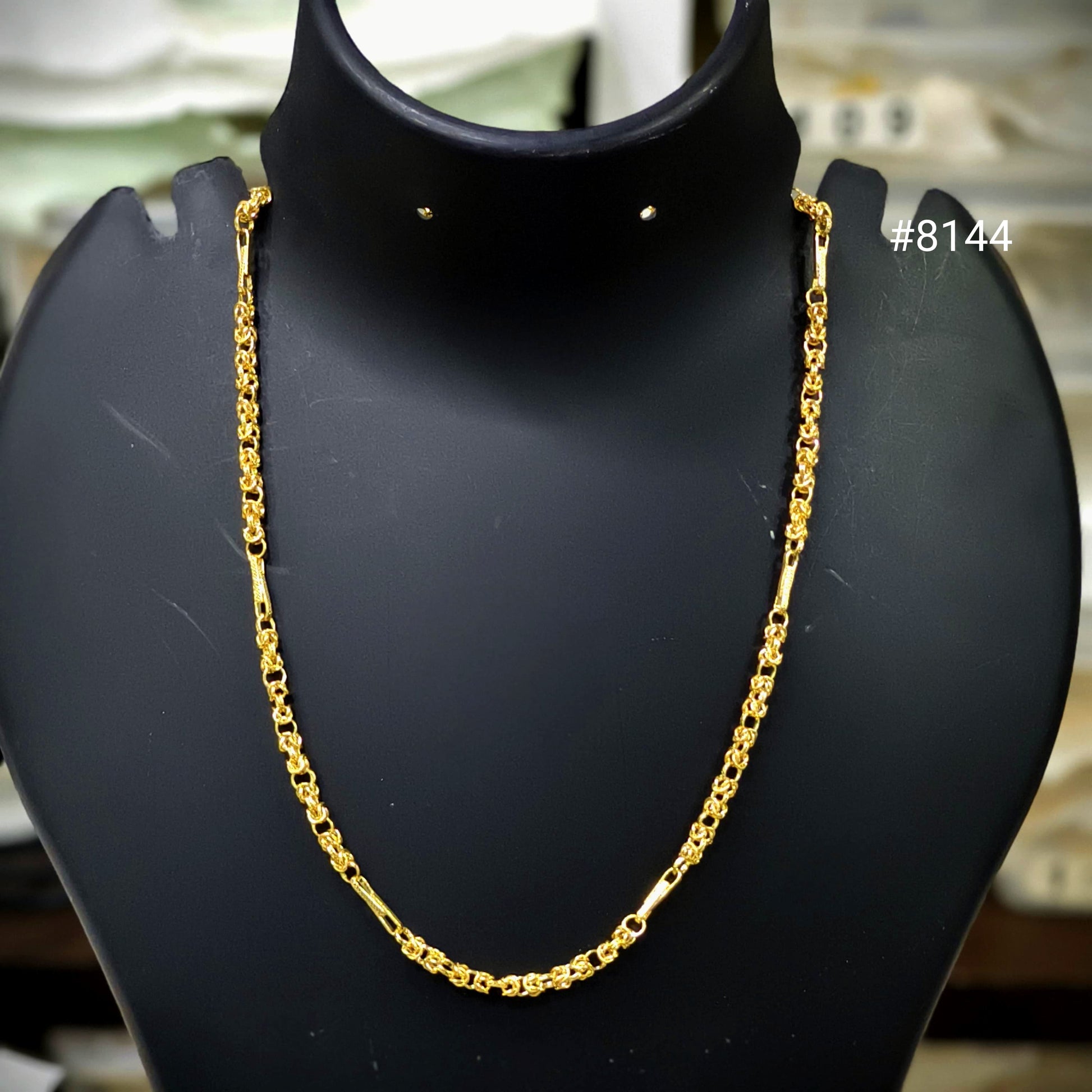 Gold chain necklace on a black mannequin bust with a blurred background.