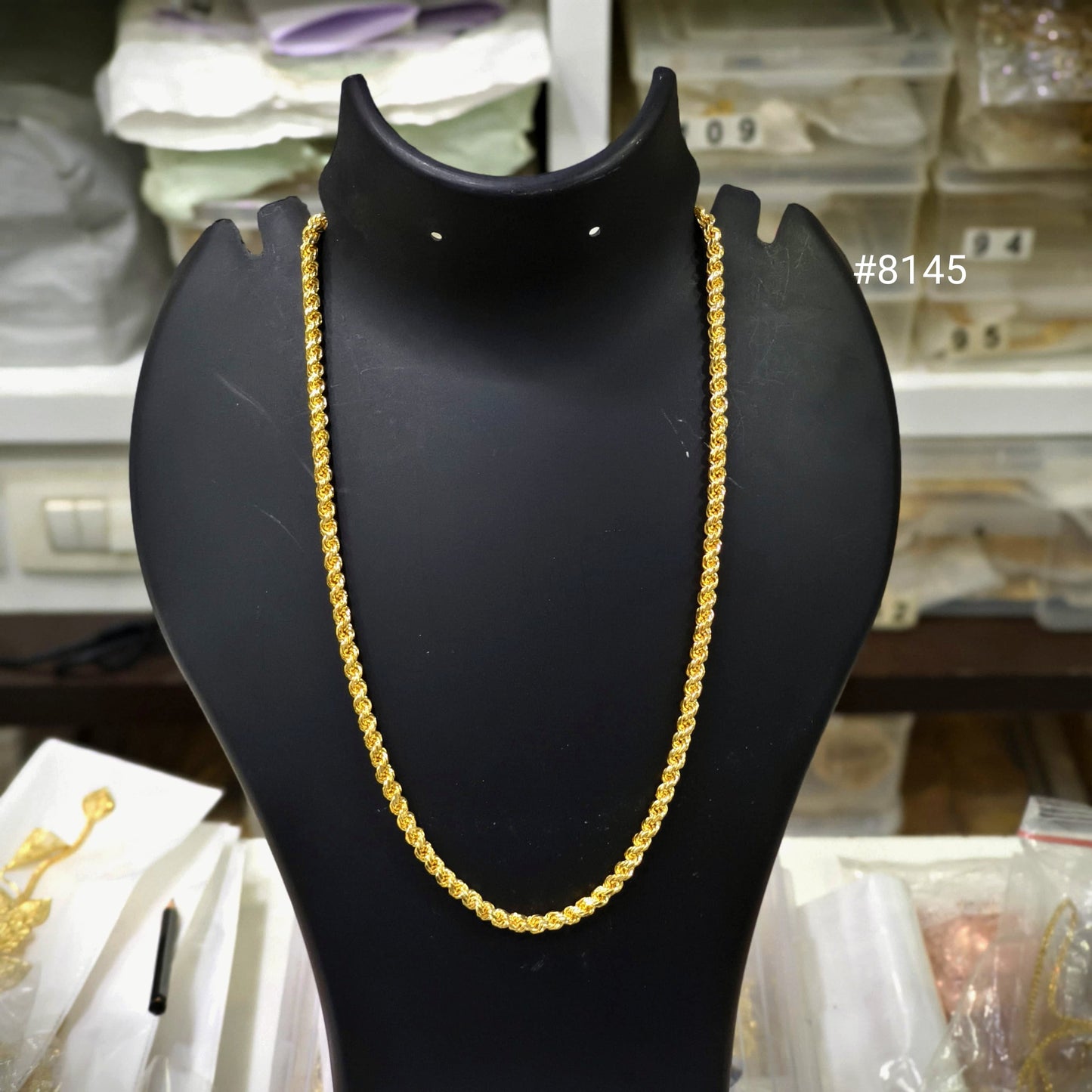 Gold chain on a black mannequin bust with a blurred background of shelves.