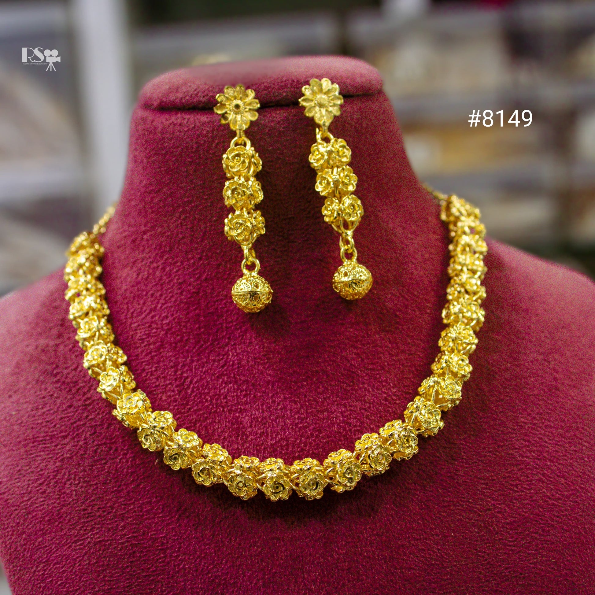 Gold necklace and earrings set on a red cushion with a blurred background