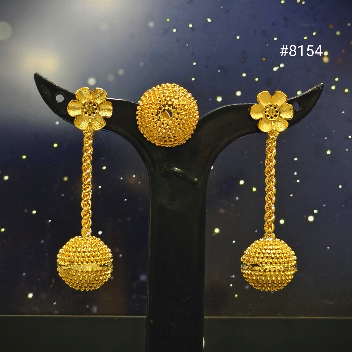 Gold earrings on a black stand with a dark, starry background