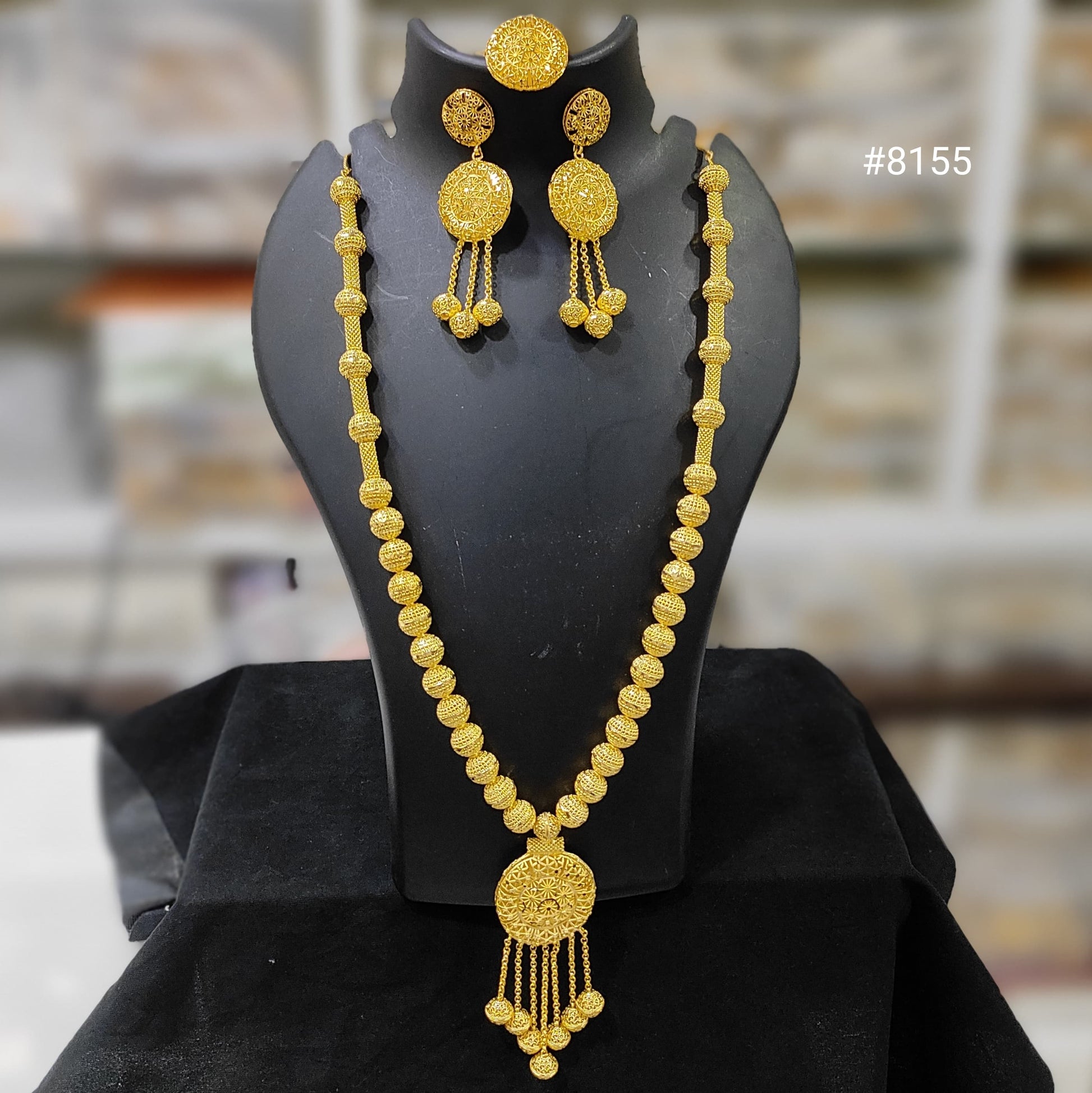 Gold necklace and earrings set on a black mannequin bust with a blurred background.