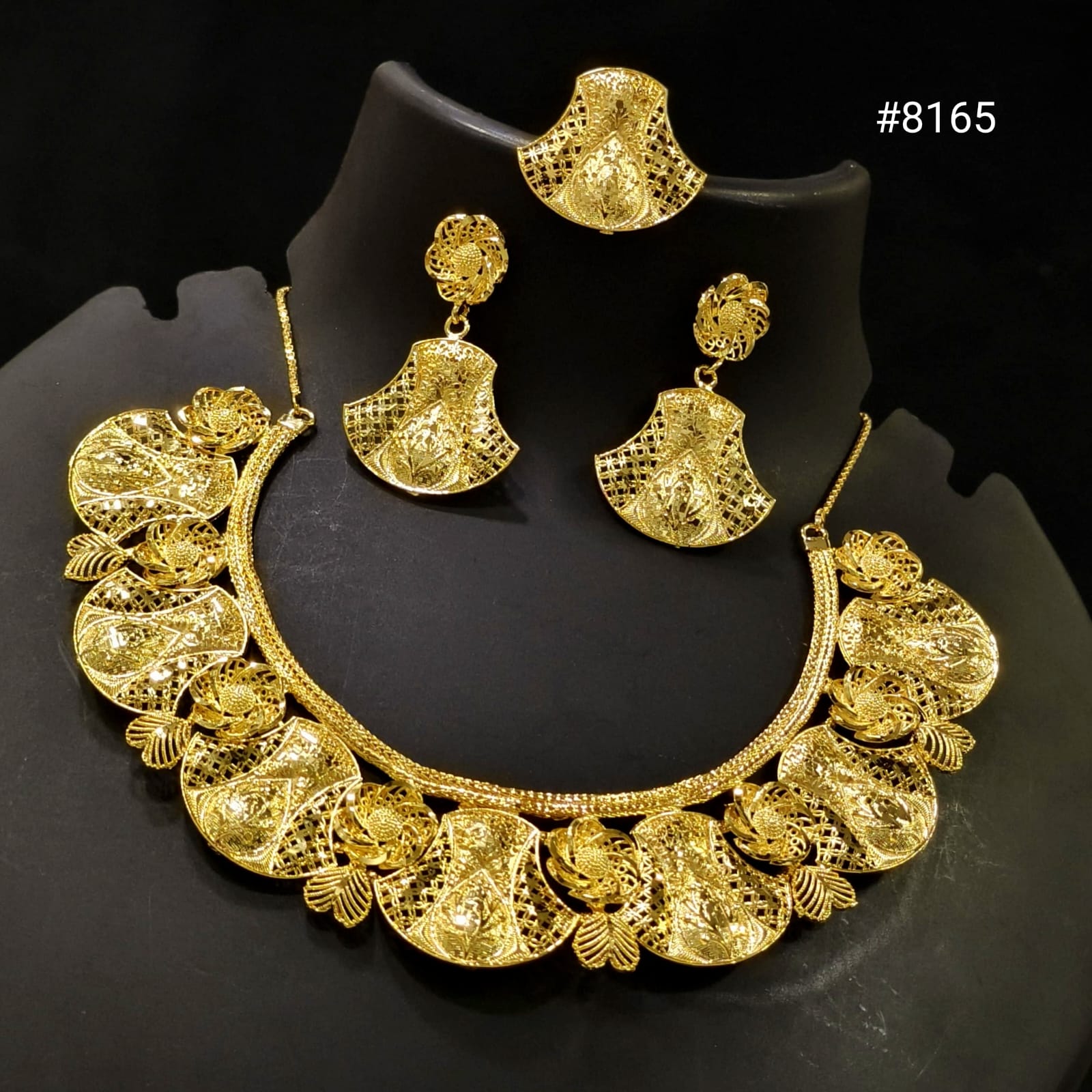 Gold necklace and earrings set on a black stand with a dark background