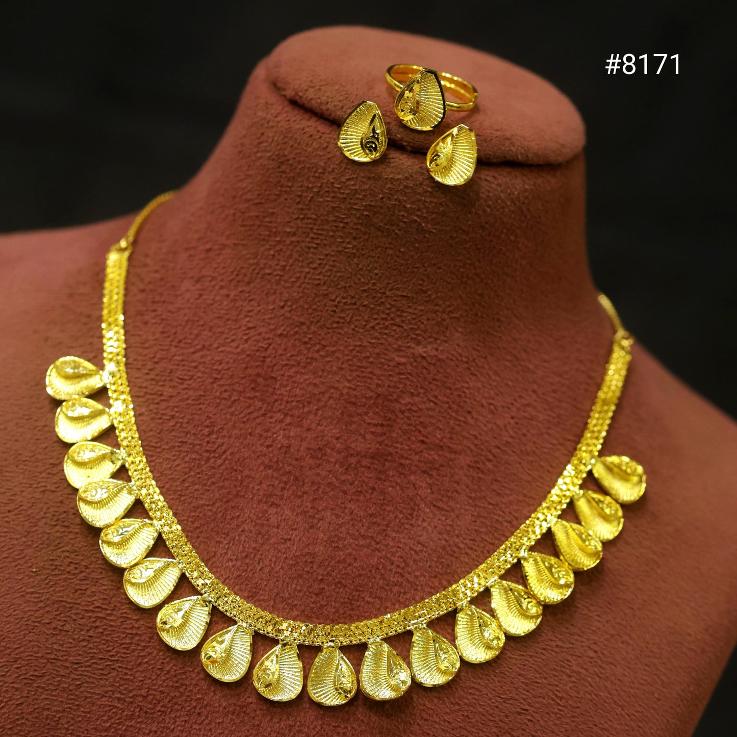 Gold necklace and earrings on a brown velvet stand with a dark background.
