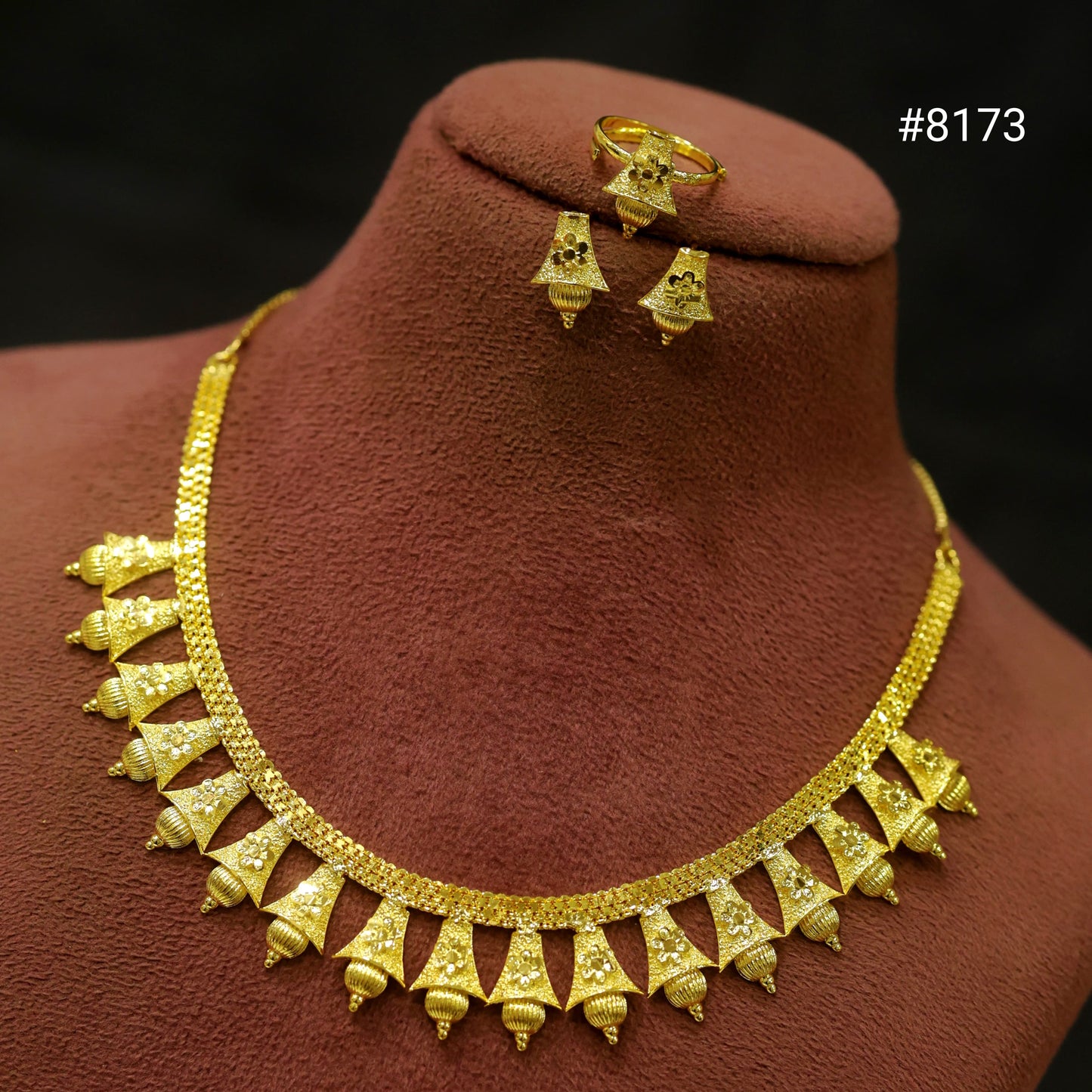 Gold necklace and earrings set on a brown mannequin bust with a dark background.