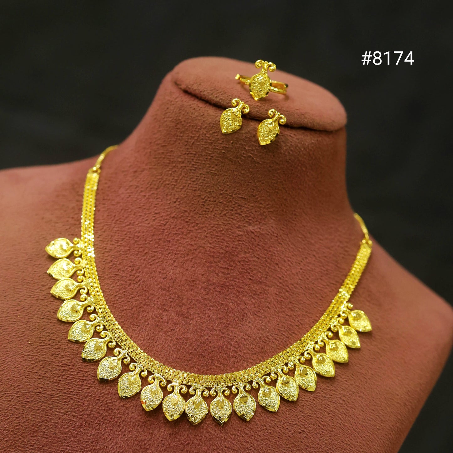 Gold necklace, earrings, and ring set on a brown mannequin bust with a dark background.