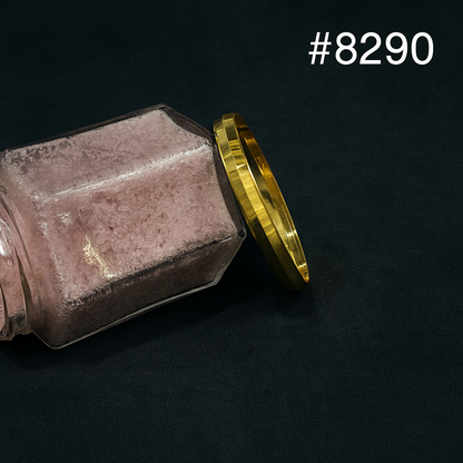 Close-up of a tipped glass jar filled with dusty pink powder beside a shiny gold lid on black fabric; product label #8290 visible.