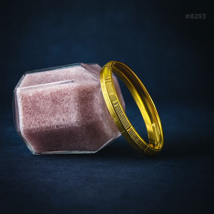 A faceted glass jar filled with pink powder lies beside two ornate gold bangles on a dark blue background, creating a luxurious mood.