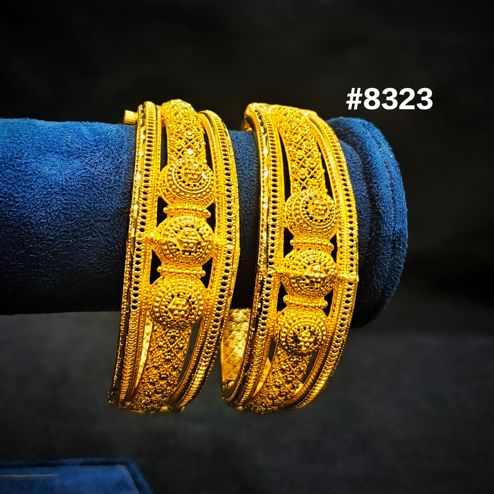 Pair of gold bangles on a blue cushion with a dark background