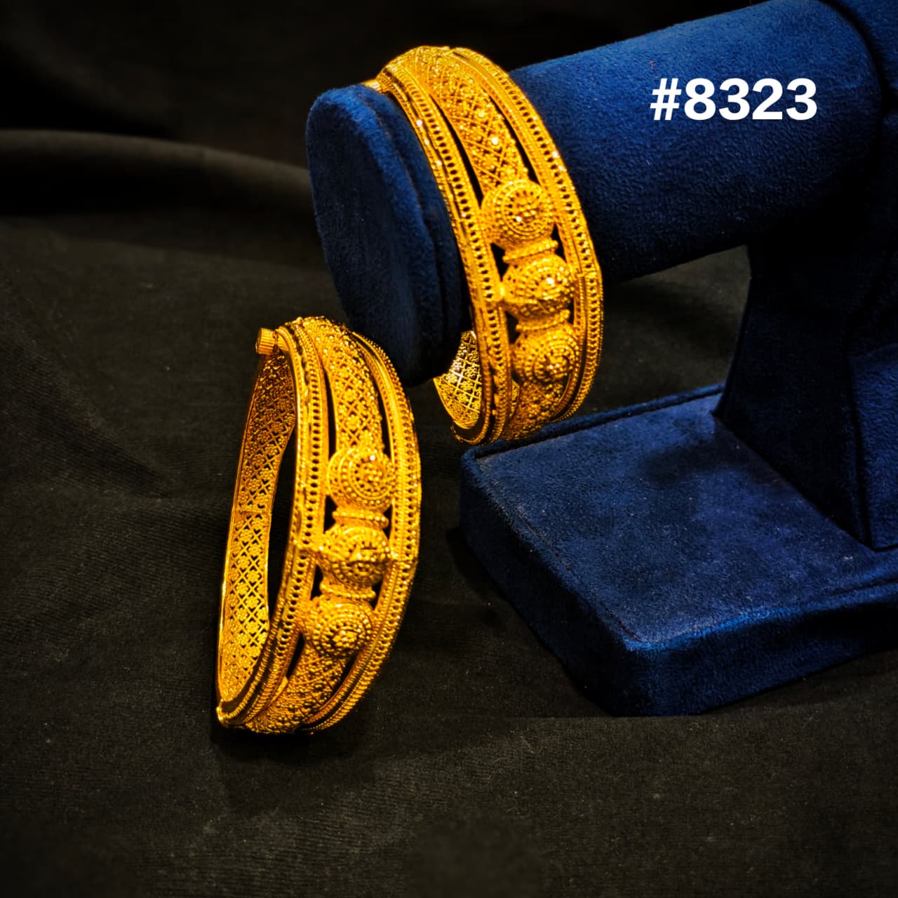 Gold bangles on a blue velvet stand against a black background