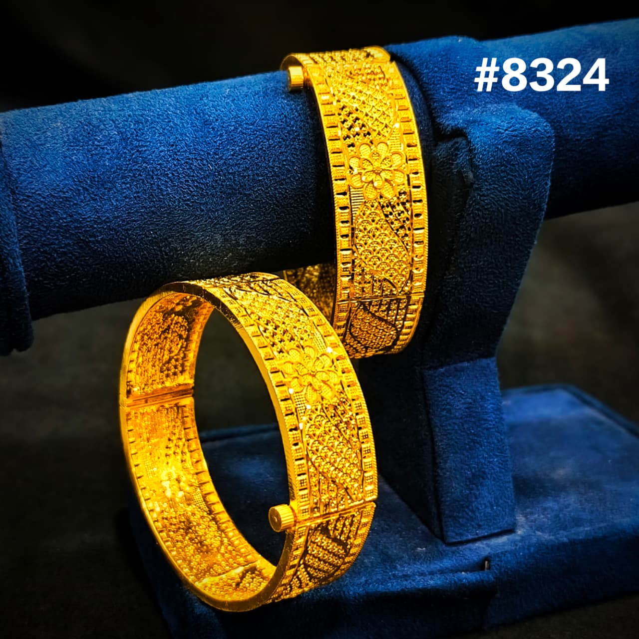 Two gold bangles on a blue stand with a dark background