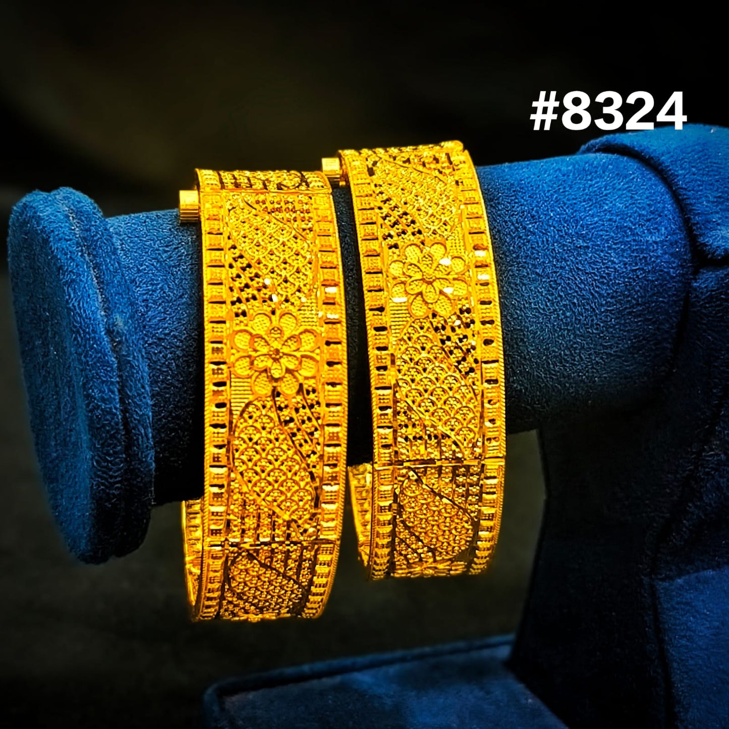 Gold bangles with intricate designs on a blue velvet stand, against a dark background.