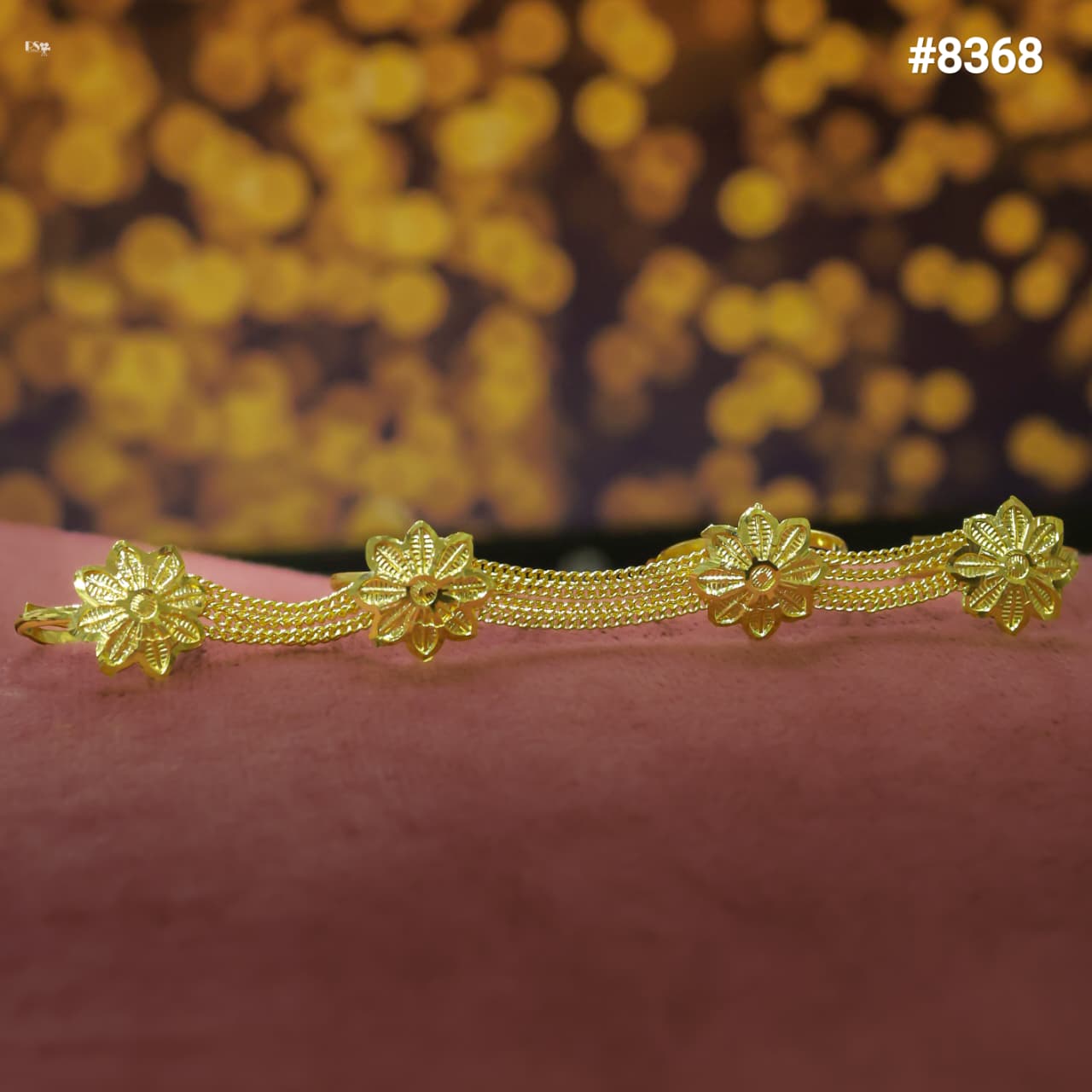 Gold finger ring with floral designs on a pink surface and blurred gold background