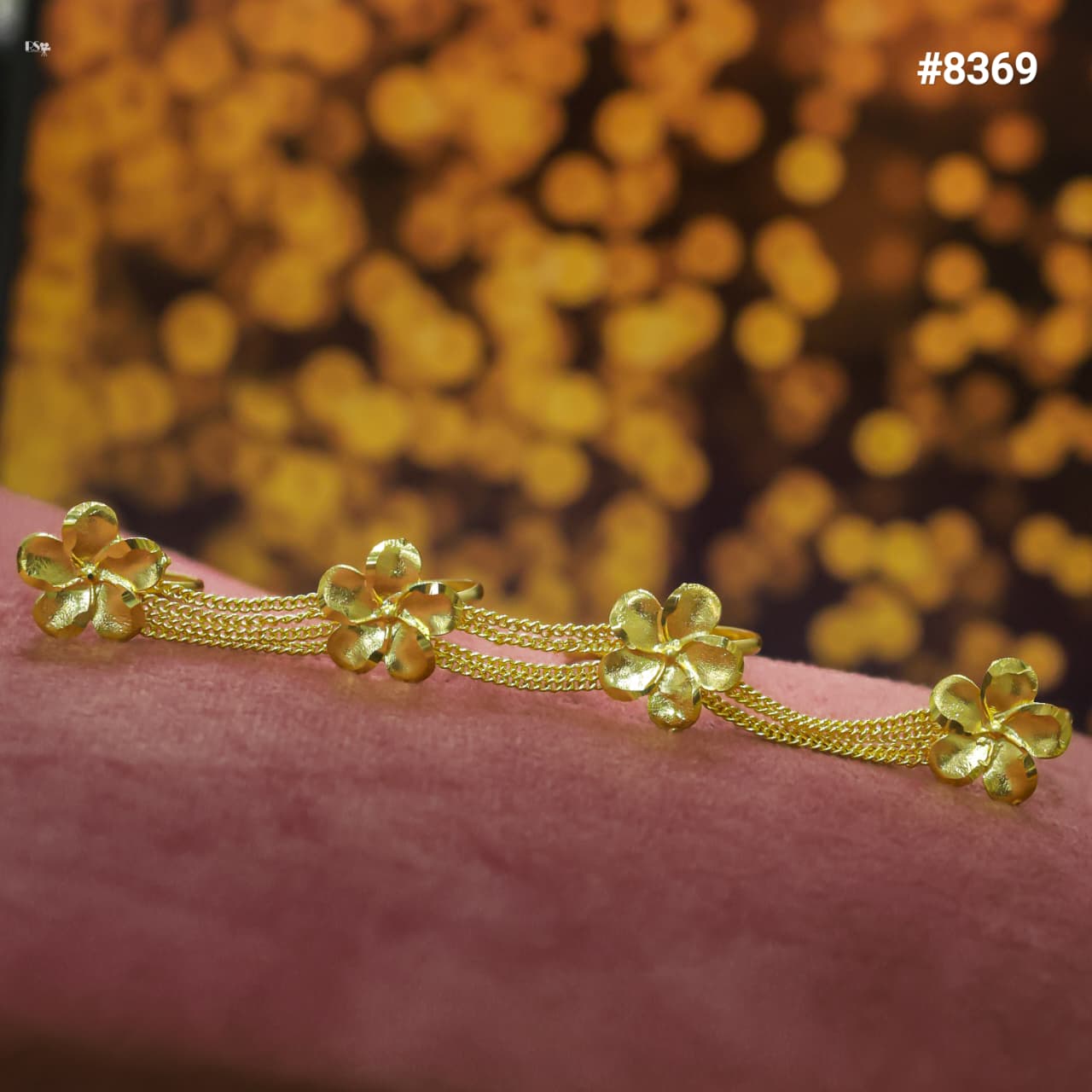 Gold Finger Ring with floral designs on a pink surface and blurred golden background