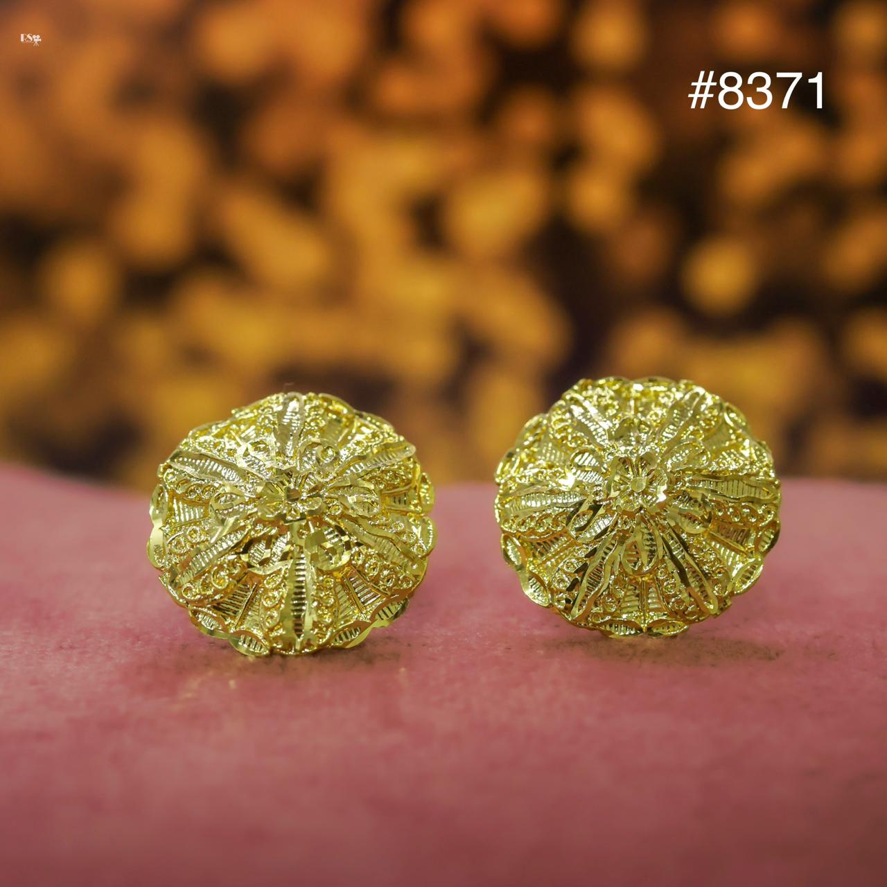 Pair of gold earrings on a pink surface with a blurred floral background