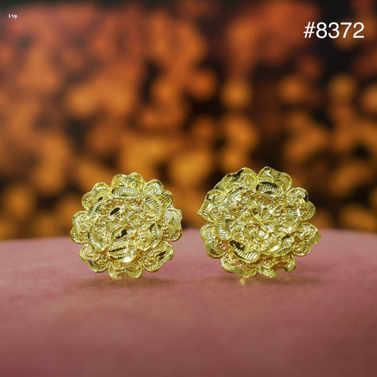 Pair of gold floral earrings on a pink surface with a blurred brown background.