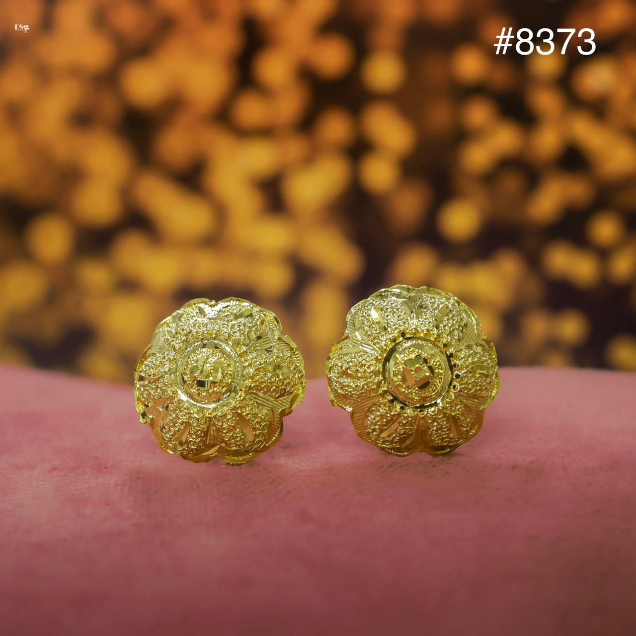 Gold floral earrings on a pink surface with a blurred gold background