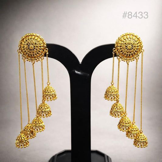 Pair of ornate gold chandelier earrings on a black stand, featuring intricate filigree discs, dangling chains, and bell-shaped charms.