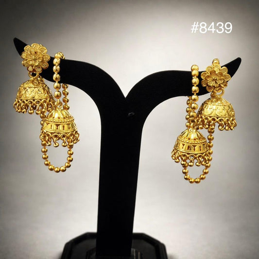 Pair of ornate gold jhumka earrings on a black stand, featuring floral tops, domed bells, dangling bead chains, and an elegant traditional design.