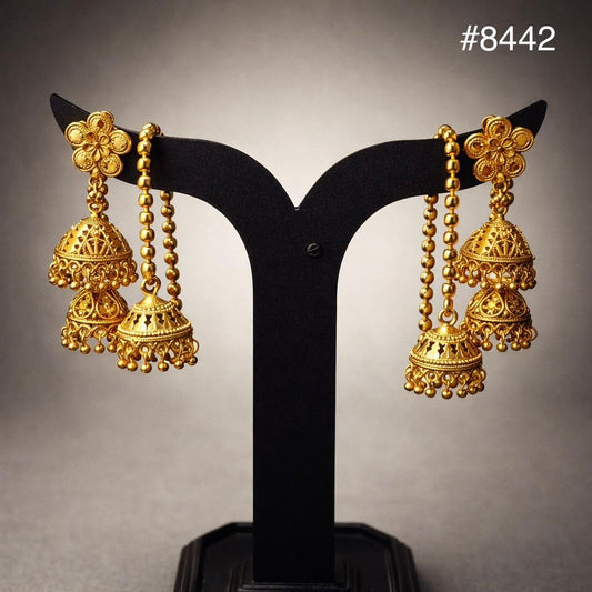 Ornate gold jhumka earrings with floral tops, beaded chains, and bell-shaped dangling charms, displayed on a black stand; elegant tone.