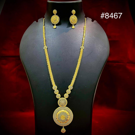 Gold jewelry set #8467 displayed on a black mannequin: ornate long necklace with circular pendant and matching earrings against a red backdrop.