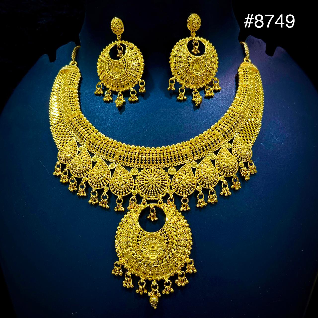Ornate gold necklace set with intricate patterns and matching circular earrings displayed on a dark mannequin, evoking elegance and luxury.