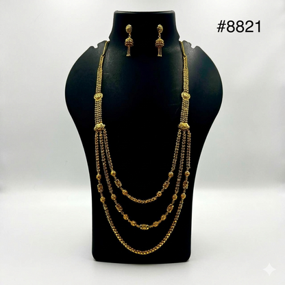 Elegant gold necklace and earrings set displayed on a black bust. The necklace features three layered chains with intricate bead patterns, exuding luxury.