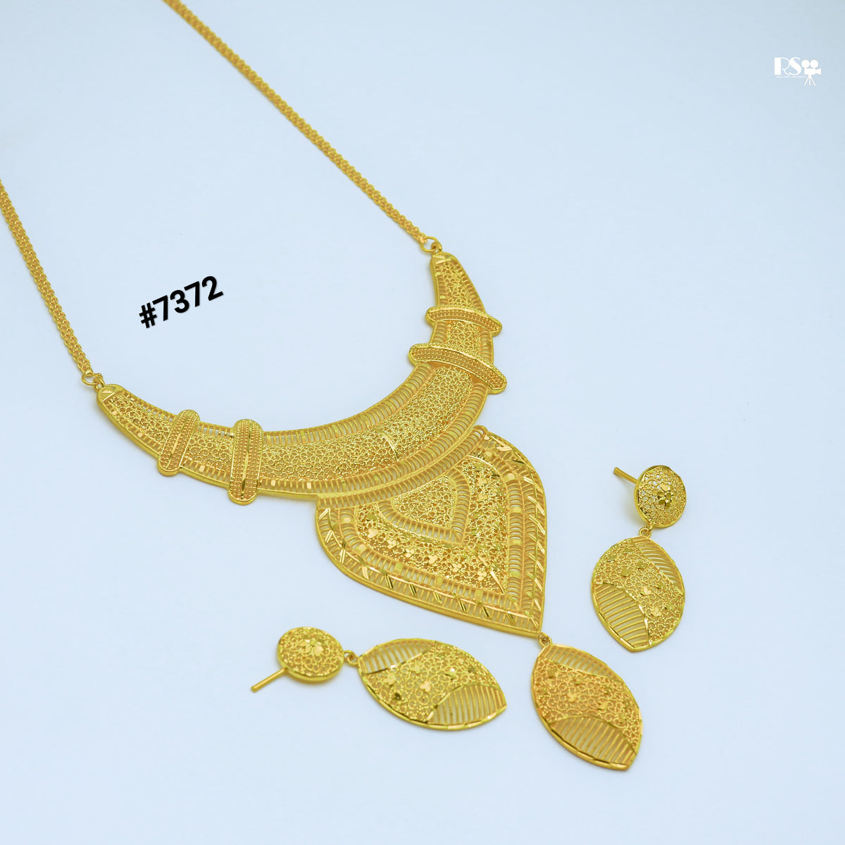 Ornate gold necklace and matching dangling earrings, featuring intricate traditional filigree patterns, arranged on a pale blue background.