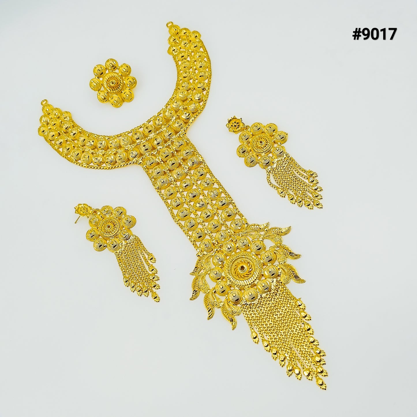 A gold jewelry set featuring a wide, textured necklace with a long, ornate pendant, matching floral earrings, and a small matching circular brooch. 2
