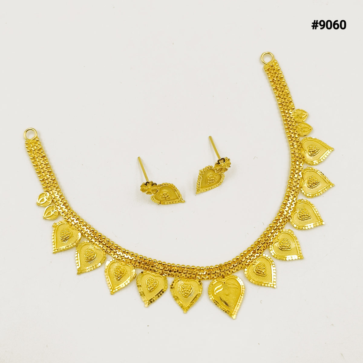 Gold traditional jewelry set on a white background: ornate necklace with heart-shaped pendants and matching dangling earrings, elegant and festive.
