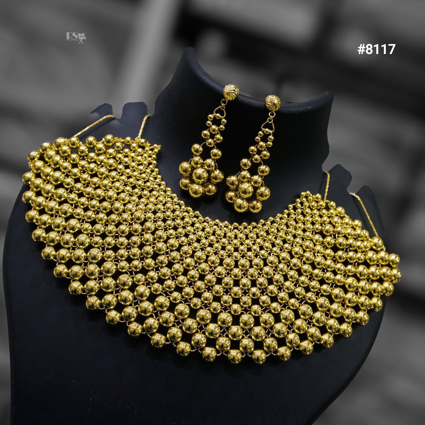 Gold beaded necklace and earrings on a black stand with a blurred background